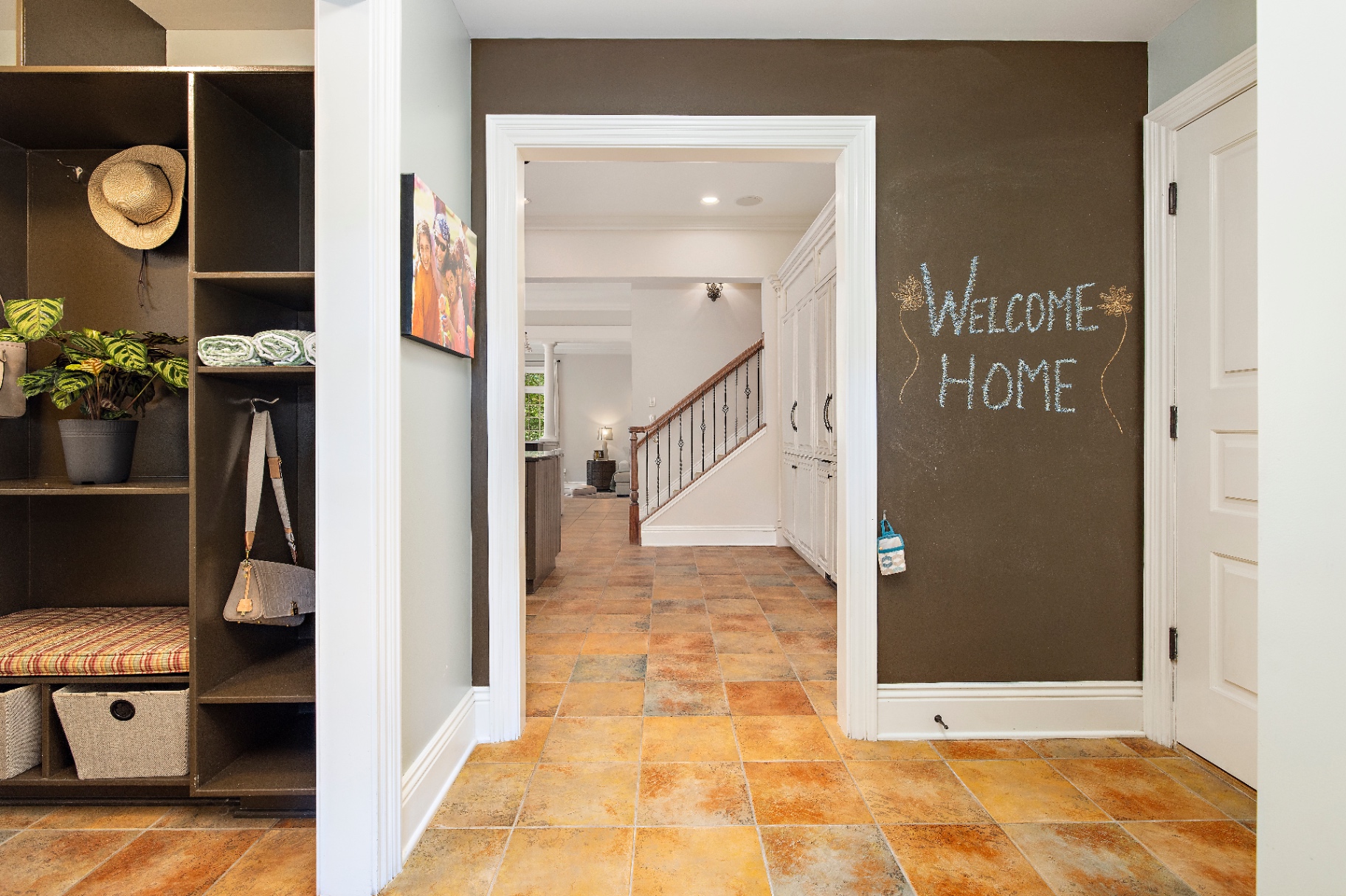 Mudroom lockers with cubbies, hooks, and bench looking through to the back staircase and 'Welcome Home' chalkboard wall