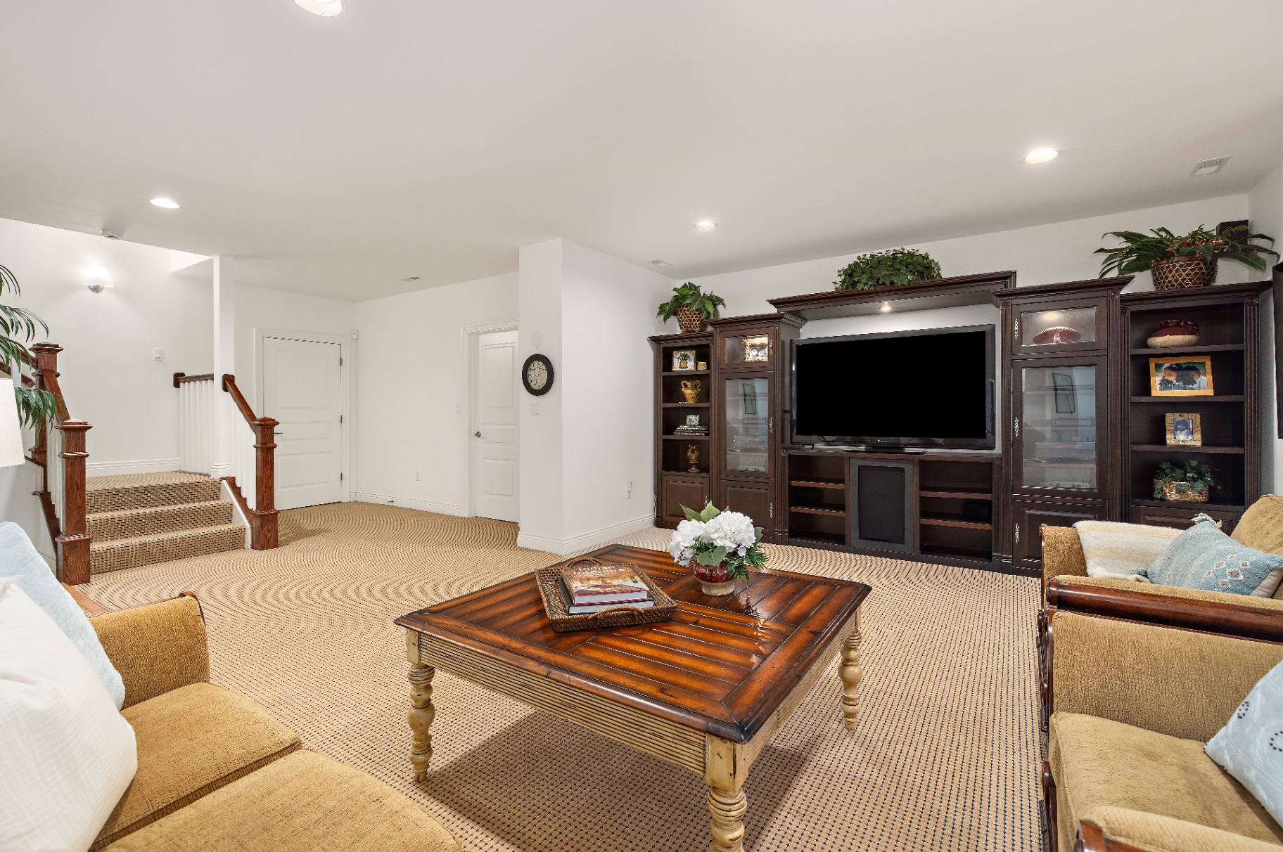 Lower level great room with dark built-in entertainment center, plush seating, and stair landing
