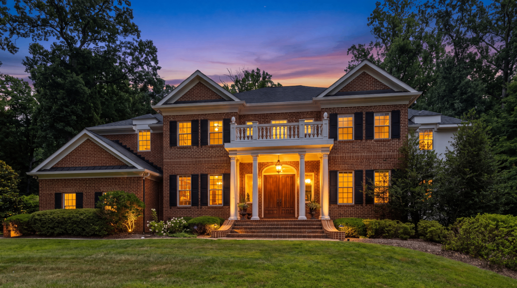 Front elevation of the brick Georgian at twilight with warm interior light glowing through every window