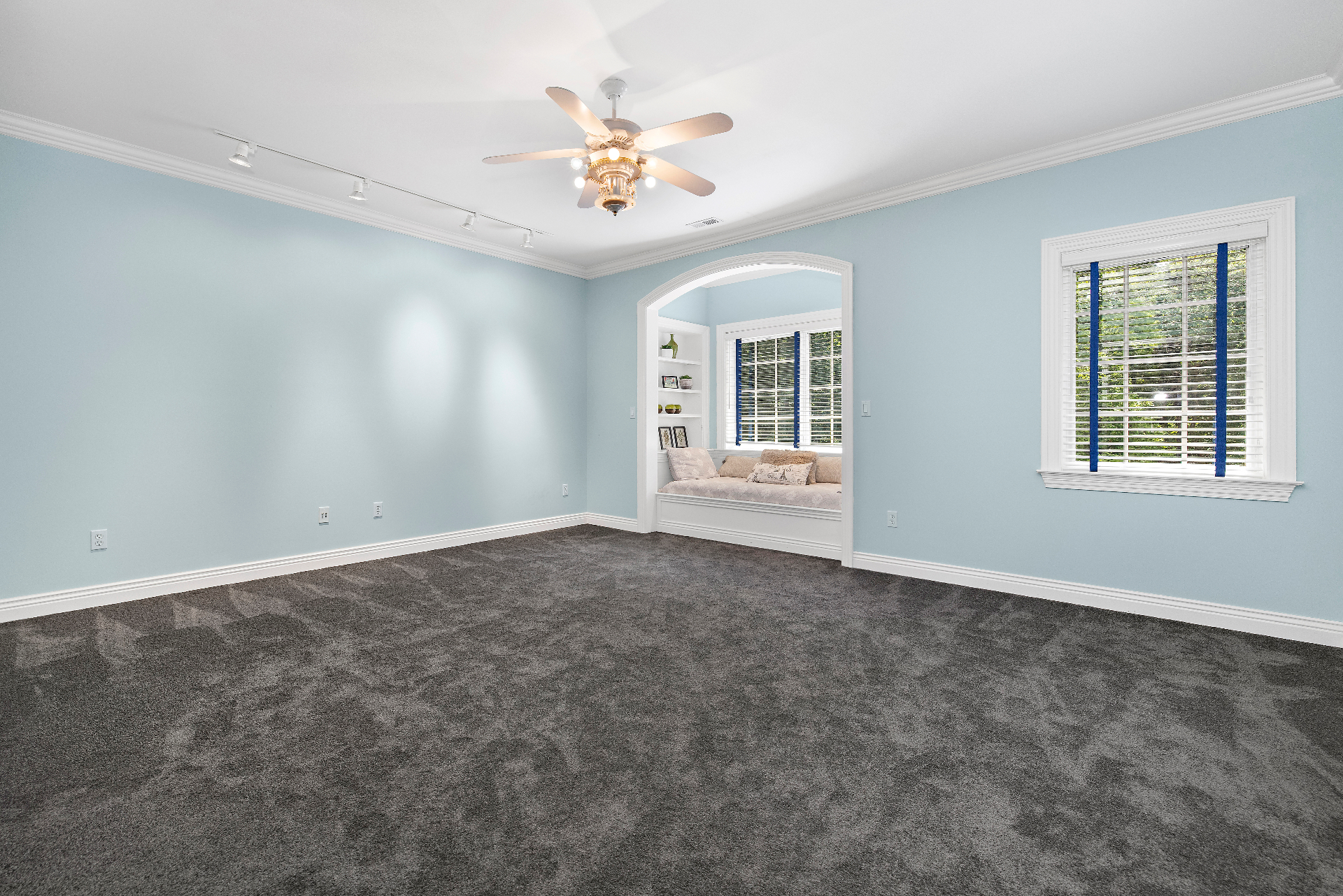 Upper floor rec room with soft blue walls, plush carpet, arched window-seat nook, and flexible open layout