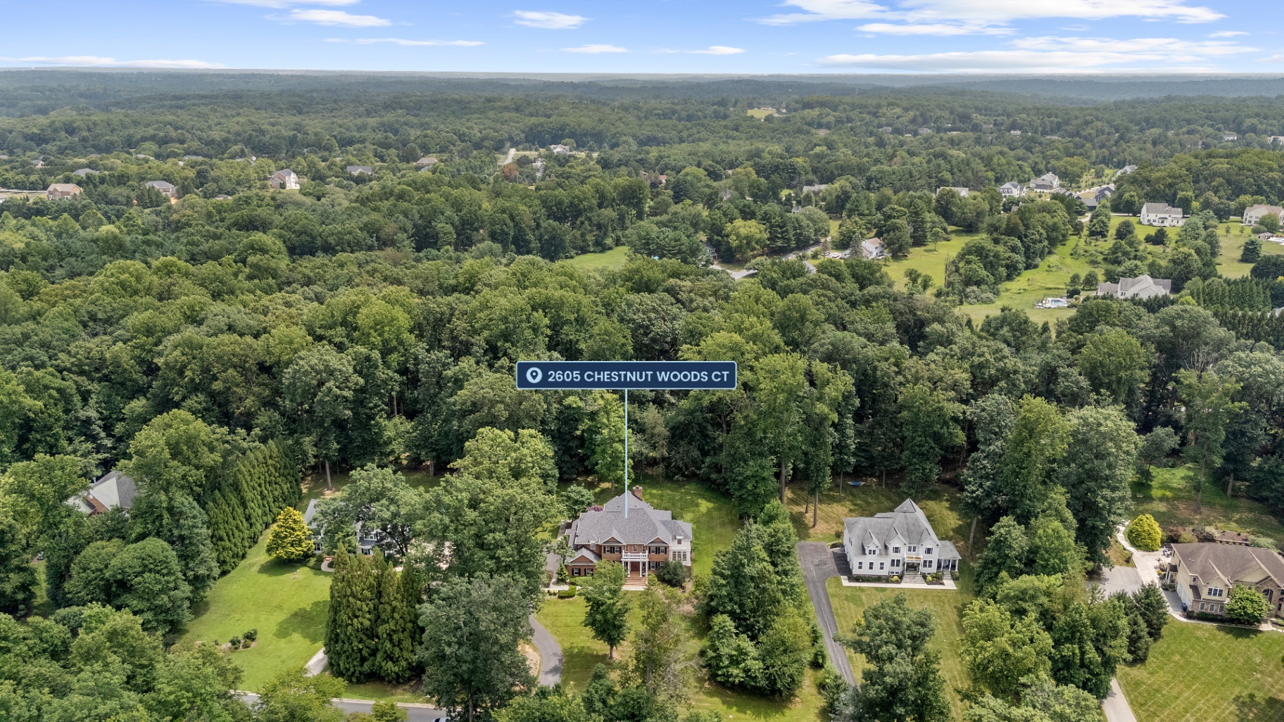 High aerial with a location pin marking 2605 Chestnut Woods Ct, showing the home nestled in the tree canopy with the neighborhood beyond